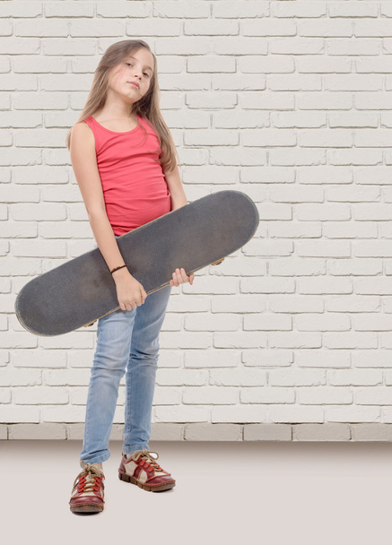 όμορφο κοριτσάκι με skateboard, λευκό φόντο τοίχο τούβλου  - Φωτογραφία, εικόνα