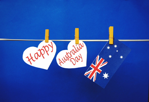 Celebrate Australia Day holiday on January 26 with a Happy message greeting written across white hearts, Australian flag hanging on pegs ( clothespin ) against red background. Toned collage - Foto, imagen