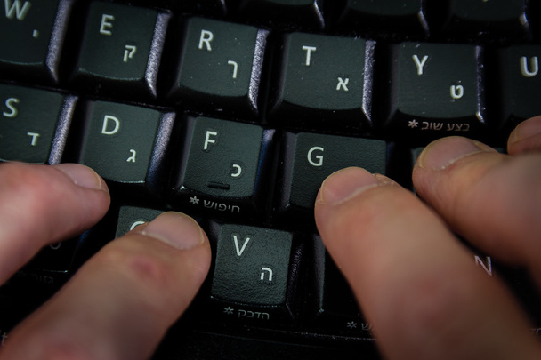 Człowiek, wpisując na klawiaturze litery w języku hebrajskim i angielskim - Zdjęcie, obraz