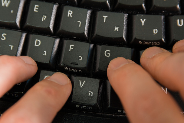 Homem digitando em um teclado com letras em hebraico e inglês
 - Foto, Imagem