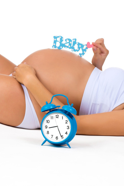 Happy pregnancy. Pregnant belly with alarm clock. Soon birth. Fetal development by months - Foto, Imagem