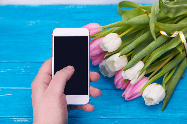 Man hand holding smartphone against spring tulips - Photo, Image