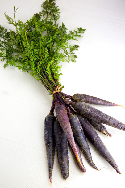 Bunch of heirloom purple carrots, over white and wooden backgrou - Photo, Image