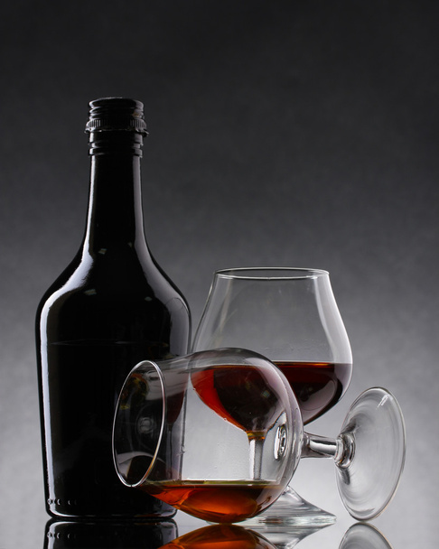 Glasses of brandy and bottle on gray background - Foto, Bild