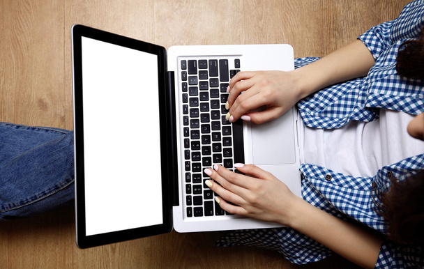 Laptop in girls hands typing and sitting on a wooden floor - Φωτογραφία, εικόνα
