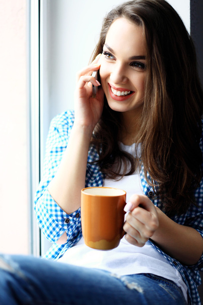 Pretty peaceful young woman using cell phone and drinking coffee - Foto, imagen
