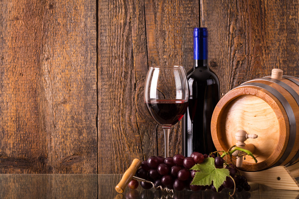 Copa de vino tinto con botella de barril de uvas y fondo de madera
 - Foto, Imagen