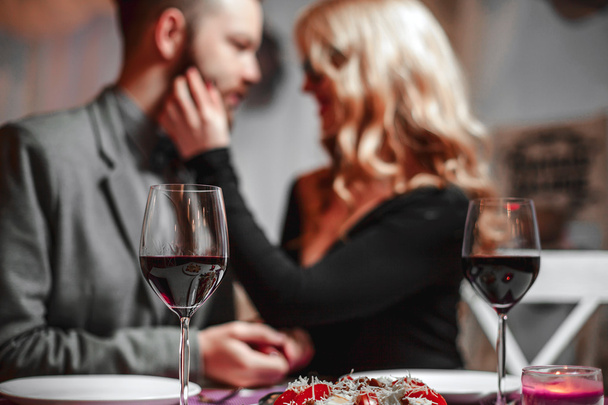 Beautiful young couple with glasses of red wine in luxury restaurant - Zdjęcie, obraz