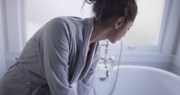 Красива молода іспаномовна жінка сидить на ванні тестує воду
 - Фото, зображення