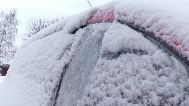 Tyttö puhdistaa lunta punaisessa autossa. Toimintaa hidastettuna. Oikea puoli
. - Materiaali, video