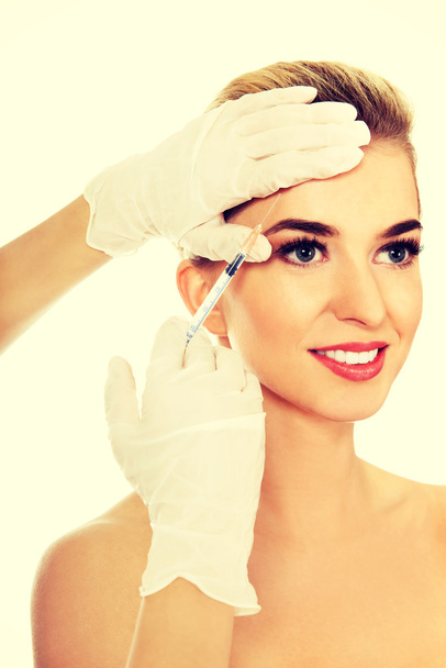 junge lächelnde Frau bekommt Botox ins Gesicht gespritzt - Foto, Bild