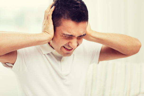 Несчастный человек закрывает уши руками дома
 - Фото, изображение