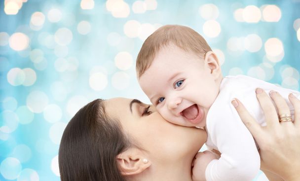 happy mother kissing her baby over blue lights - 写真・画像