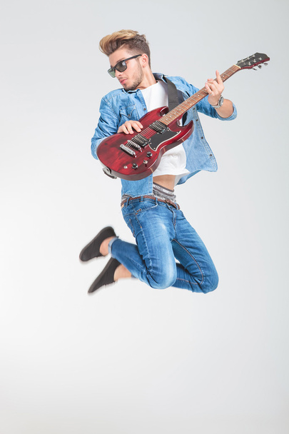 artiste masculin sautant en studio tout en jouant de la guitare
 - Photo, image