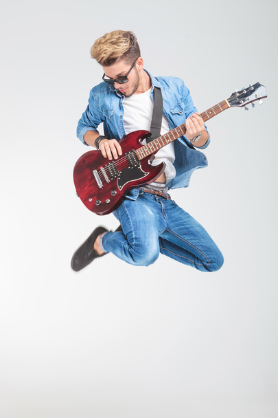 artist jumping in studio while playing guitar - Foto, Imagen