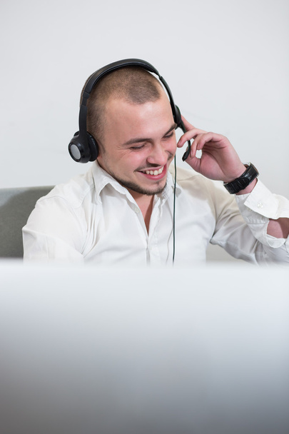Smiling casual young man with headset using computer in a bright - Zdjęcie, obraz