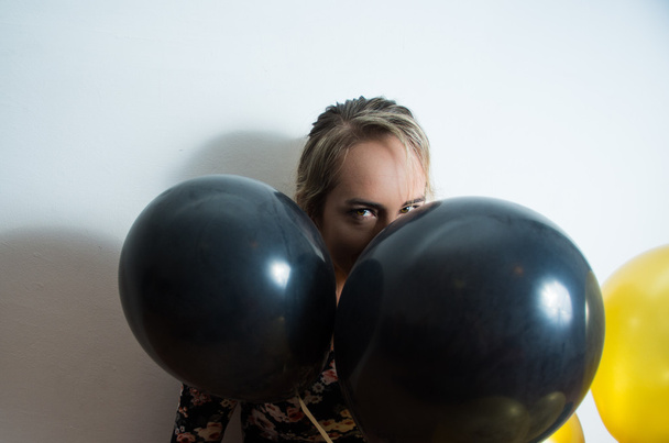 Beautiful model leaning back against white wall and peeking head out from balloons - Foto, imagen