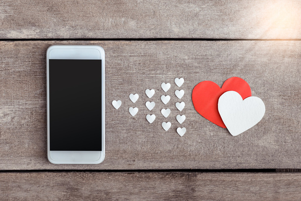 Smartphone and hearts paper on wooden background - Фото, изображение