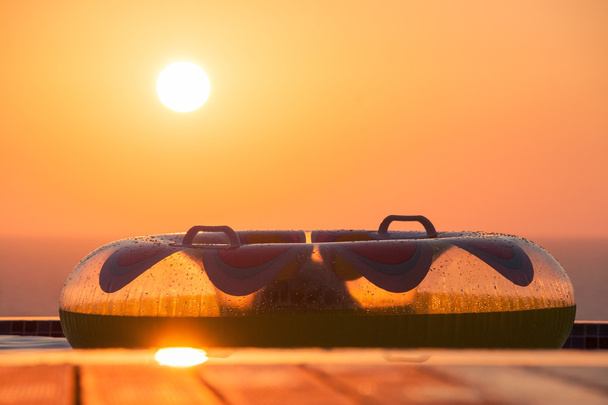Φουσκωτά κολύμπι δαχτυλίδι σε ένα κατάστρωμα πισίνα, με θέα θάλασσα στον Πωμό με τον ήλιο να δύει - Φωτογραφία, εικόνα