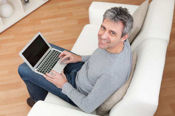 Senior man sitting in sofa and using laptop - Foto, afbeelding