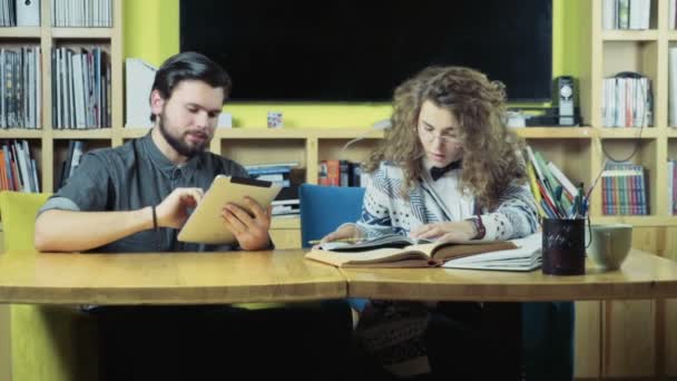 mužské student pomocí tabletu vedle žena čtení knihy zpomalené - Záběry, video