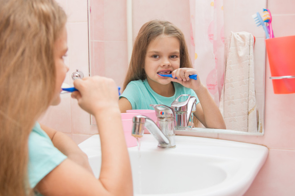 Six year old girl cleans teeth side looking in the mirror in the bathroom - Фото, зображення