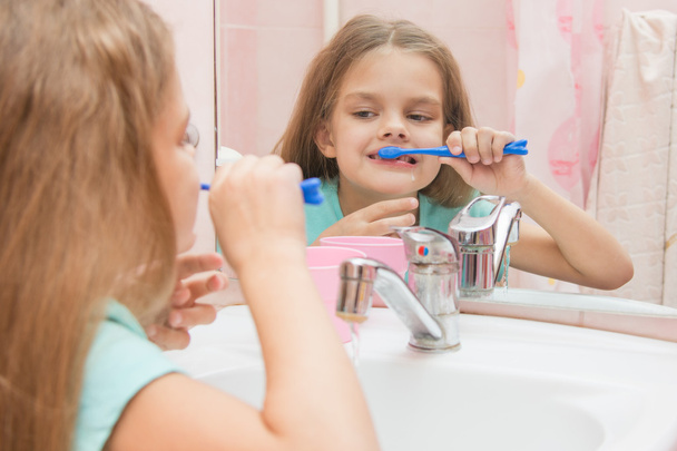 Шестилетняя девочка веселится, чистя зубы. Посмотри в зеркало в ванной.
 - Фото, изображение