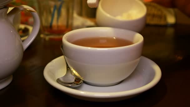 Přidání kusový cukr s kleštěmi na černý čaj v poháru - Záběry, video