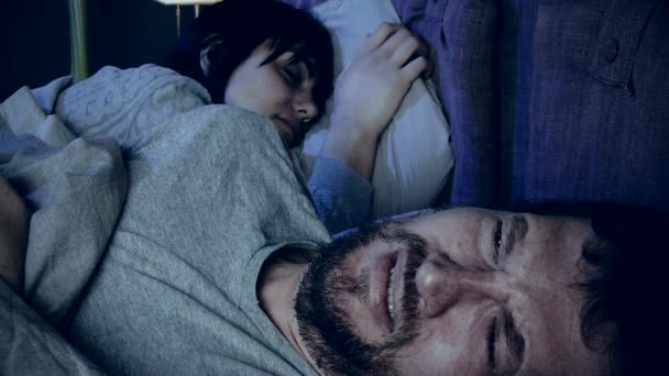 Hombre sintiendo dolor mientras está acostado en la cama con la esposa dormida en el dormitorio - Imágenes, Vídeo