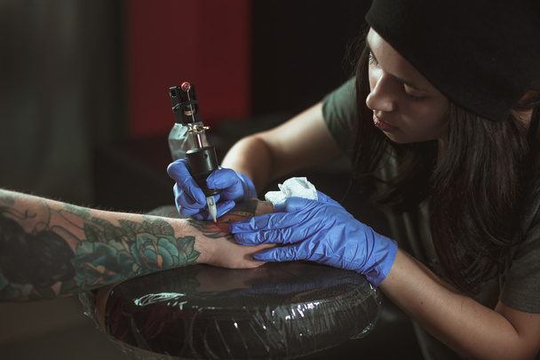 Beautiful brunette girl makes tattoo. Tattooist makes a tattoo. Closeup - Zdjęcie, obraz