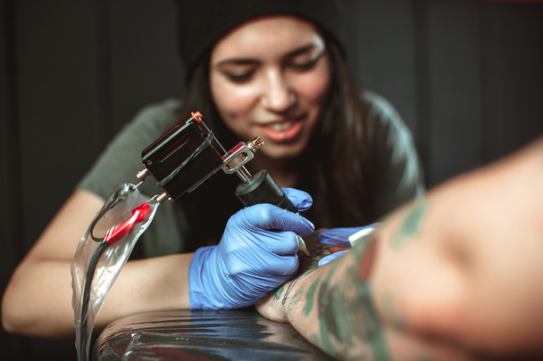 Beautiful brunette girl makes tattoo. Tattooist makes a tattoo. Closeup - Photo, Image