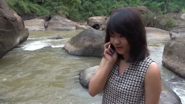 Привлекательная женщина разговаривает по мобильному телефону у прекрасного водопада
. - Кадры, видео