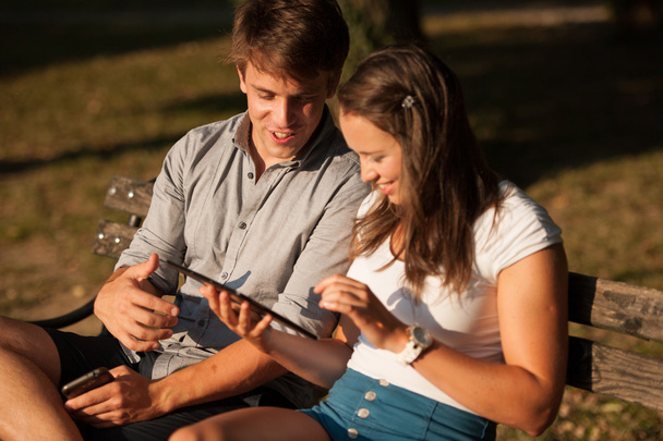 Young couple having fun on a bench in park while socializing ove - Foto, Bild
