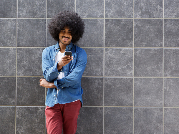 Smiling black man standing with mobile phone outside - Photo, image