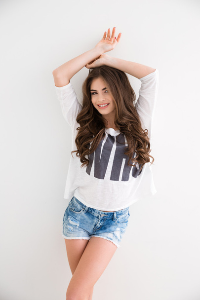 Cheerful happy young woman in jeans shorts standing and smiling  - Fotó, kép