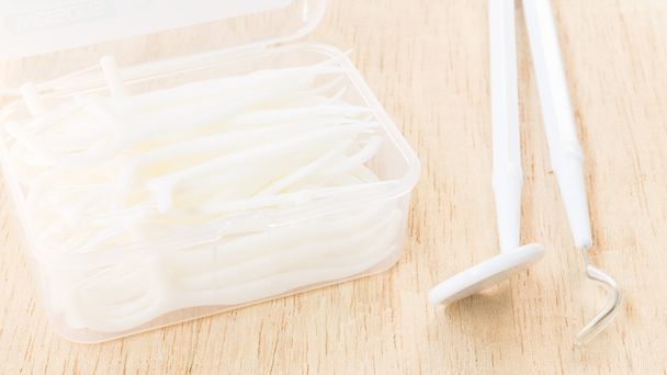 Усні пристрої: коробка білої зубної нитки на дерев'яному фоні
 - Фото, зображення