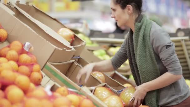 Young woman chooses ripe pomelo on store shelves. - Video, Çekim
