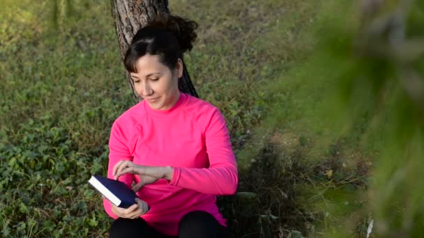 Valkoihoinen nainen lukemassa kirjaa puistossa
 - Materiaali, video