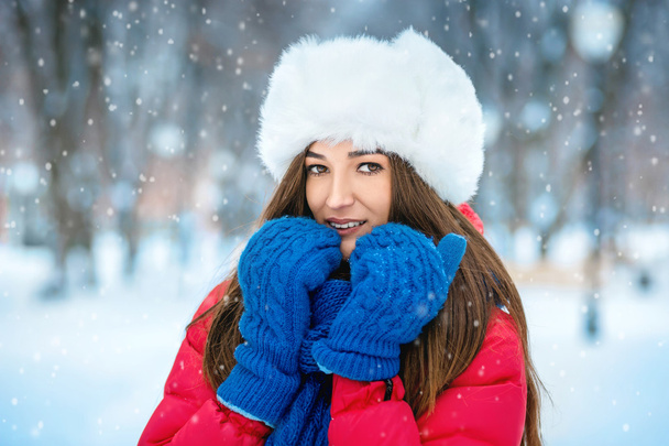 A girl in a white fur hat covers her face with her hands dressed in blue mittens. - Fotoğraf, Görsel