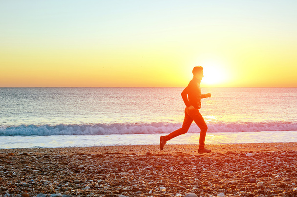 молодой человек бежит на пляже против моря и голубого неба ранним утром
  - Фото, изображение