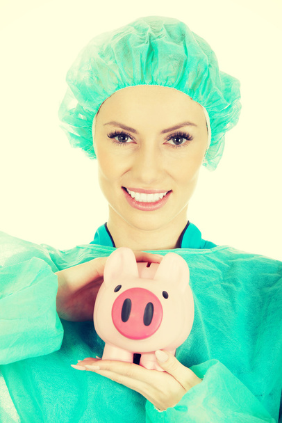 Female doctor with pink piggy bank. - Zdjęcie, obraz