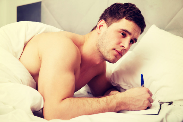 Man writing a note in his bed. - Fotó, kép
