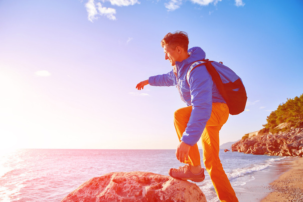 traveler with backpack standing on the cliff against sea and blue sky at early morning - Photo, image