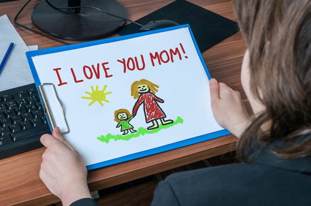 Business woman (mother) in office holds greeting card from her child with drawing and message I Love You Mom. - Photo, Image
