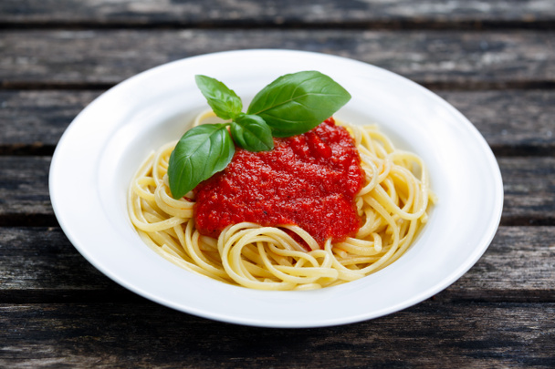 Spaghetti mit Marinara-Sauce und Basilikumblättern auf dem Holztisch. - Foto, Bild