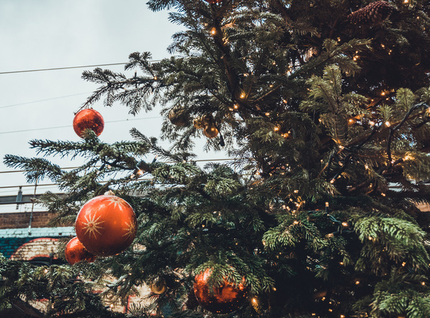 Barevné červené ozdoby visí venku na zdobeném vánočním stromečku před nákupním centrem, zblízka vánoční ples - Fotografie, Obrázek