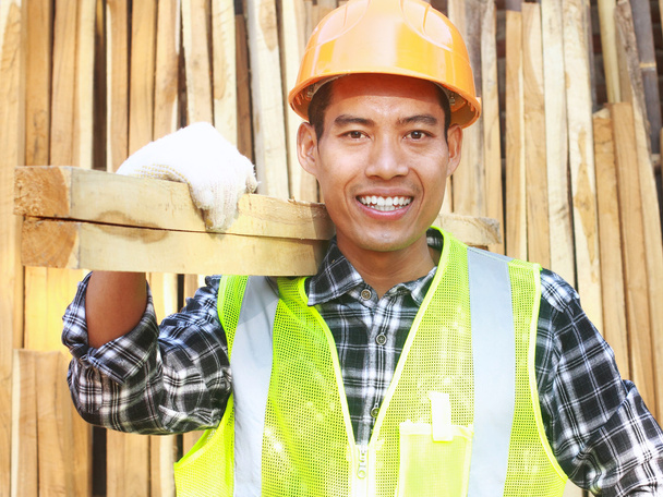 木材を運ぶヘルメットと安全ベストを持つ男性労働者 - 写真・画像