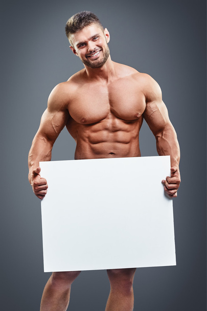 Muscular young man holding blank white poster - Φωτογραφία, εικόνα