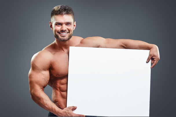 Smiling bodybuilder holding blank white poster - Fotoğraf, Görsel