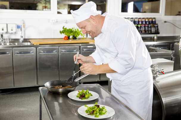 Glimlachen van chef-kok bereidt biefstuk schotel in restaurant - Foto, afbeelding